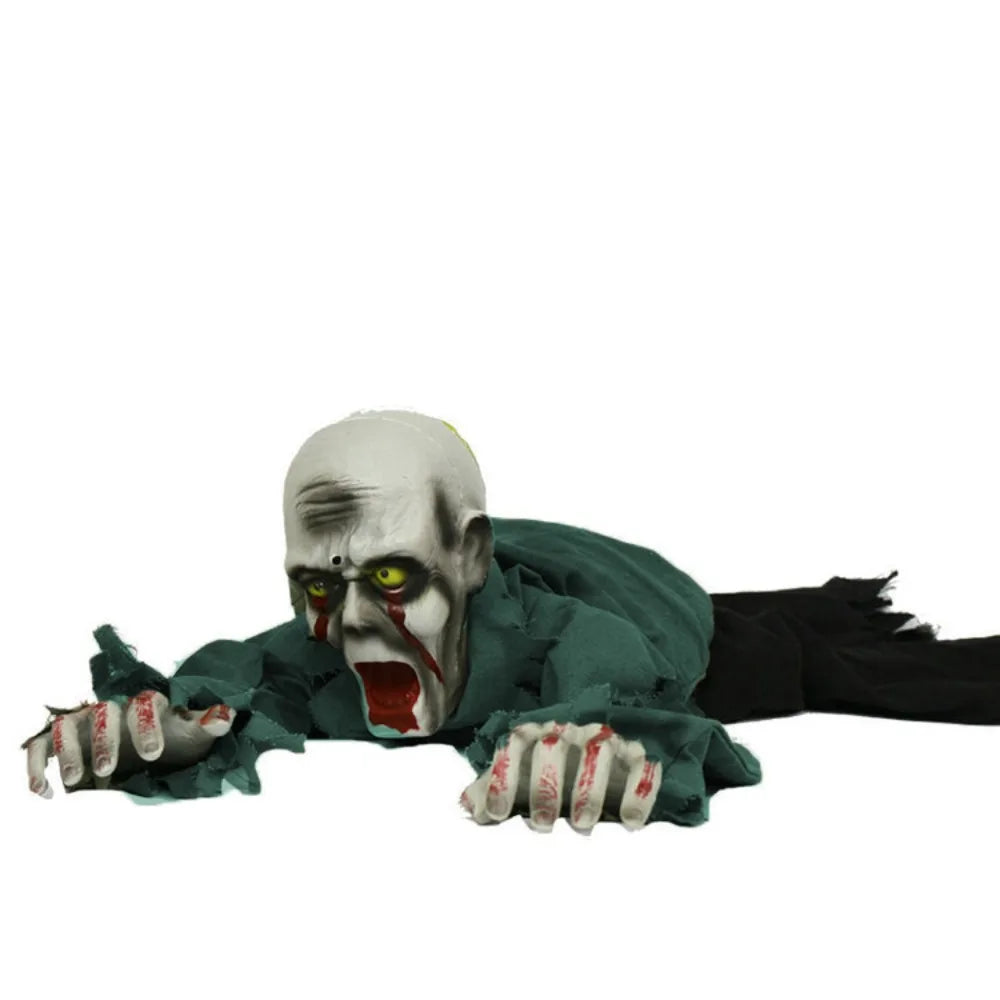 A creepy zombie Halloween decoration lying on its stomach, wearing a tattered dark green shirt and black pants, with a pale gray head, glowing yellow eyes, and bloody hands and mouth.