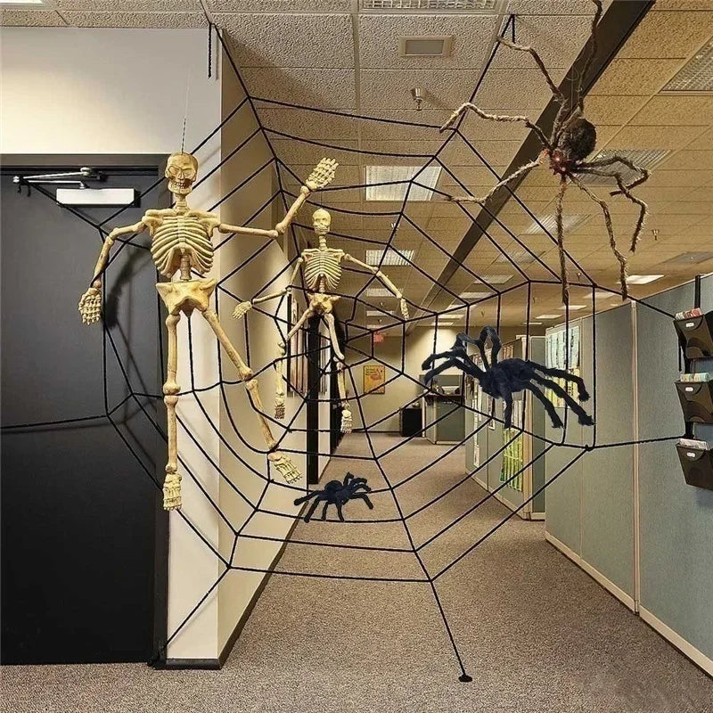 Halloween office hallway decoration with hanging skeleton figures, a large black spiderweb canopy, and several plastic spiders on a carpeted corridor.
