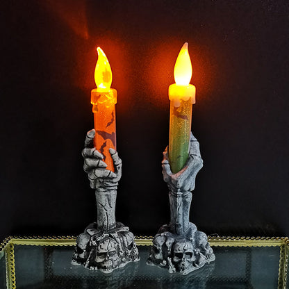 Two skeleton hand candle holders with lit candles on a dark background