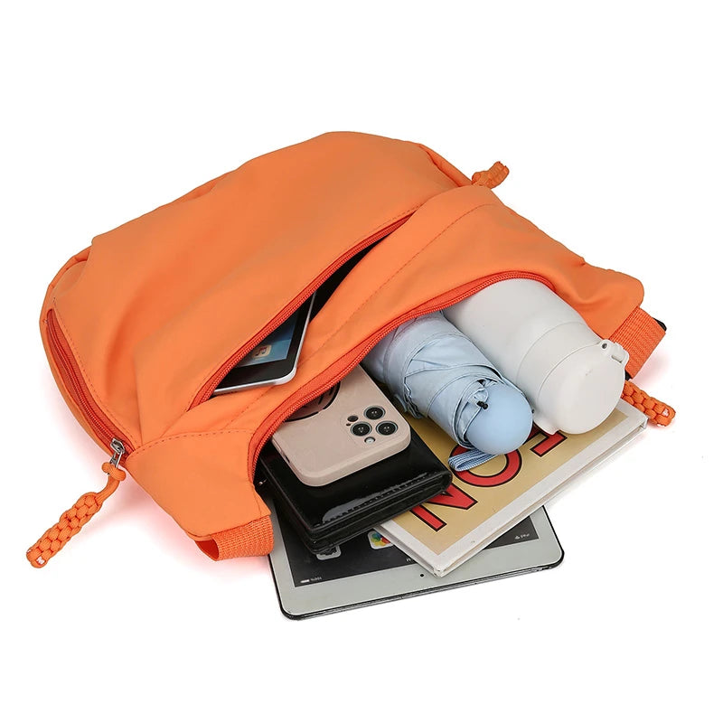 Orange drawstring bag with electronic devices and a book inside on a white background
