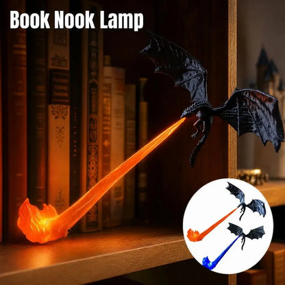 A dragon-shaped book nook lamp with a black winged dragon body and a glowing orange flame-like nook, shown on a wooden bookshelf beside books. Text at the top reads 'Book Nook Lamp,' and a circular inset shows alternate color options with blue and orange flames.