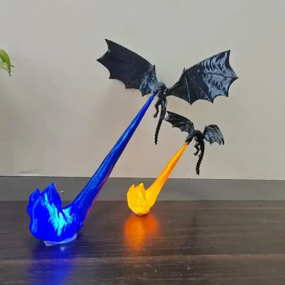 Two black dragon figurines with spread wings, each mounted on a flame-shaped base that glows blue or orange, displayed on a dark wooden surface against a plain beige wall.