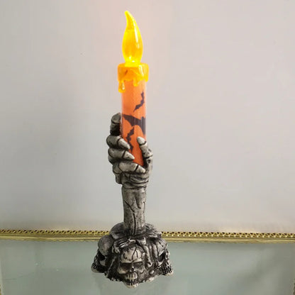 Candle holder shaped like a skeleton hand holding a candle against a plain background