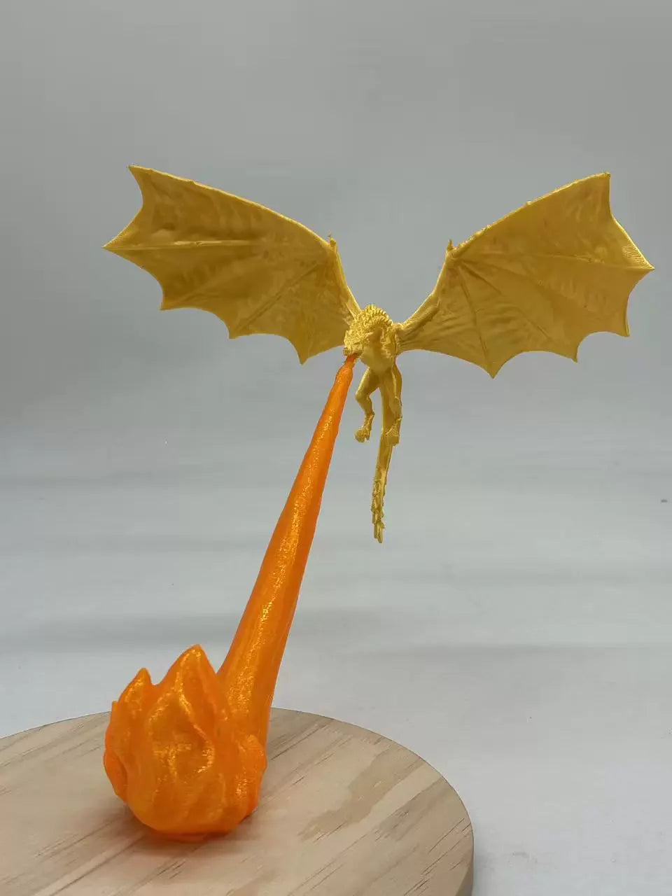 A 3D-printed fantasy dragon figurine with spread wings and a long orange tail, mounted on a round wooden display base against a plain light gray background.